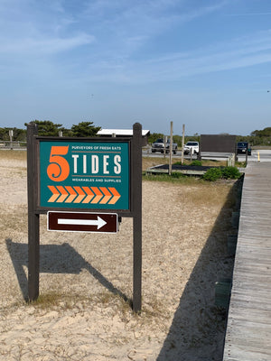 a teal directional sign with orange and white lettering for 5 Tides framed in dark wood with an arrow pointing to the right