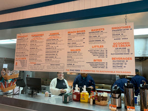 a large menu sign with a white background, orange headings and black text hanging over a restaurant's ordering area