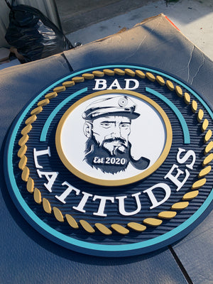 a photo of a multi-layered sign for Bad Latitudes with two shades of blue, a raised gold rope pattern, and white text 