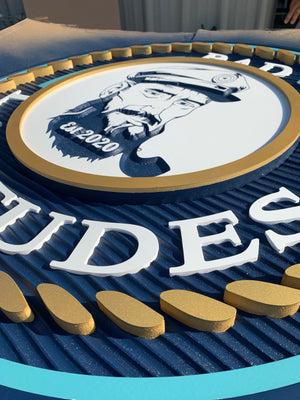 an angled closeup of a multi-layered sign for Bad Latitudes with two shades of blue, a raised gold rope pattern, and white text 