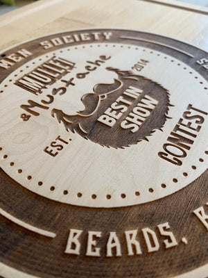 a closeup of an award for the Bearded Men Society, a circular wooden plank with laser engraved text and the logo for the Mullet & Mustache contest 