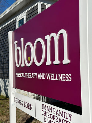 an angled photo of a purple sign with raised white lettering for Bloom Physical Therapy and Wellness