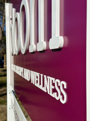 an angled photo showing the raised white lettering on a purple sign for Bloom Physical Therapy and Wellness