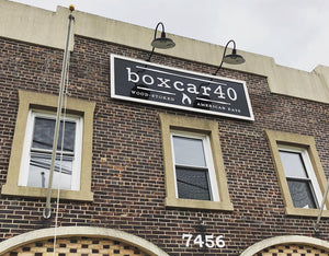 an angled photo of a black sign with a white border and lettering for boxcar40 mounted to a brick wall