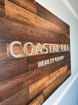 an angled closeup of a sign for Coastal Life Realty showing the raised aluminum text mounted to a wooden background