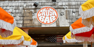 a photo of a circular sign for Crush Bar with an orange background and a white raised border and lettering mounted on a roof