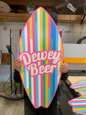 a photo of someone holding a surfboard shaped wooden sign with colorful stripes