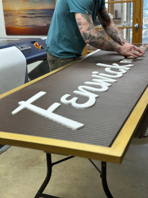 an angled photo of Justin adding the white text inserts to a rectangular brown sign with a golden border