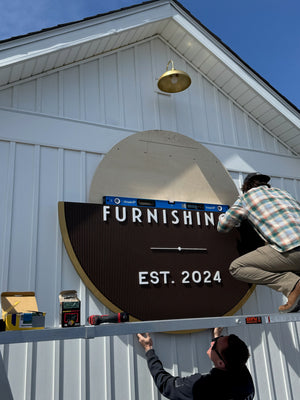 a photo of Wyatt and Justin installing half of the circular Fenwick Furnishings sign