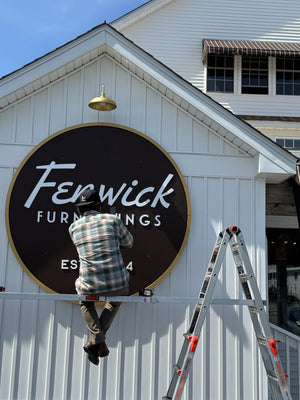 a photo of Wyatt installing the circular Fenwick Furnishings sign