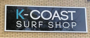 a photo of a K-Coast Surf Shop sign with a white border and lettering on a black background