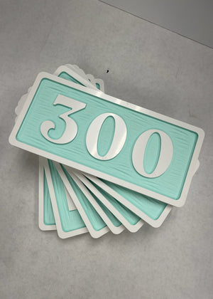 a photo of a small stack of room number signs with a white border and text on a light aquamarine background