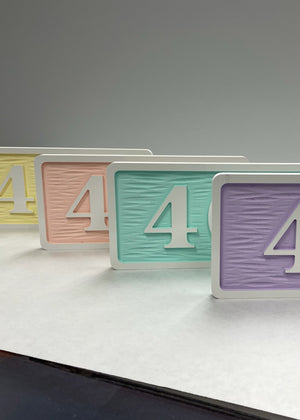 a photo of a four room number signs with white borders and text on pastel colored backgrounds
