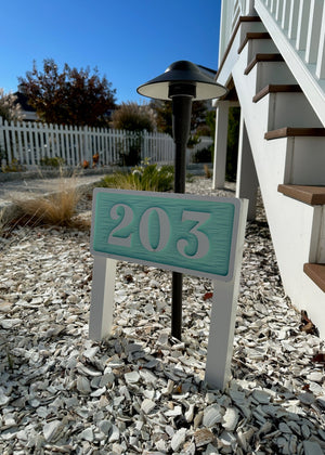 a photo of a room number sign with a white border and text on a light aquamarine background outside a cottage