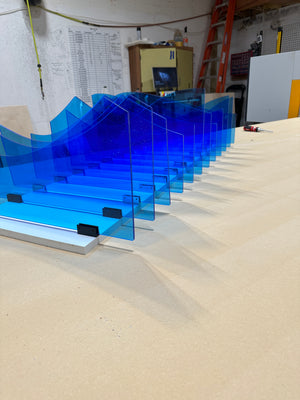 an angled photo of a part of an abstract art piece made of light blue acrylic mounted to a white plank