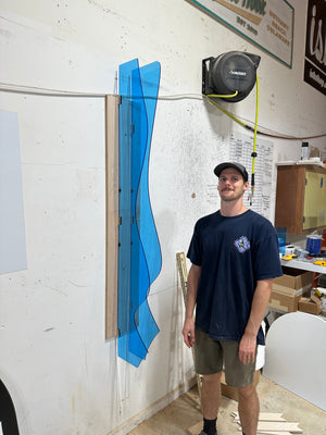 an angled photo of a part of an abstract art piece made of light blue acrylic mounted to a wall with Reeves standing next to it for scale