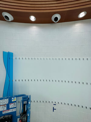 a photo of a part of an abstract art piece made of light blue acrylic being mounted to a wall