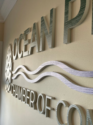 an angled photo of the Ocean Pines Chamber of Commerce lettering and logo mounted to a wall