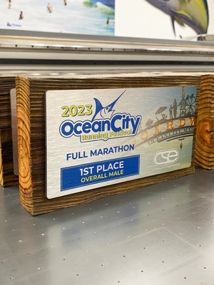 a photo of the 2023 OC Running Festival awards printed on brushed aluminum and mounted to a boardwalk wood plank