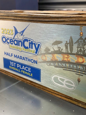 a closeup of the 2023 OC Running Festival awards printed on brushed aluminum and mounted to a boardwalk wood plank