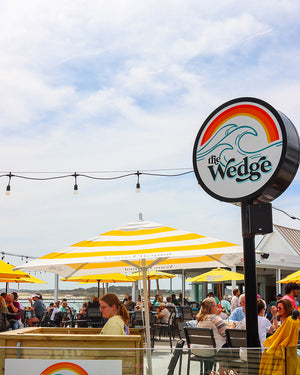 Outdoor setting with 'The Wedge' sign and people sitting under yellow umbrellas.