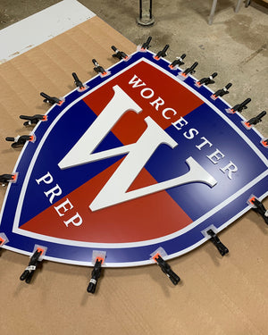 a photo of the Worcester Prep logo sign with clamps holding it while the adhesive sets