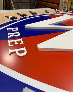 an angled closeup of the Worcester Prep logo sign with clamps holding it while the adhesive sets