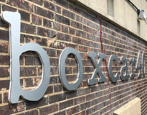 an angled closeup of aluminum lettering saying "boxcar40" mounted to a brick wall