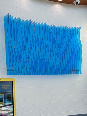 a photo of an abstract art piece made of light blue acrylic mounted to a wall