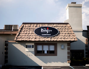 a photo of a sign for The Bonfire restaurant with a black background and white text mounted on a roof